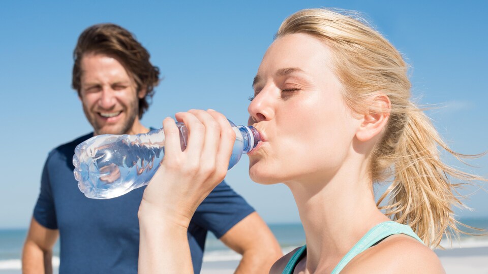 Un homme regarde une femme boire l'eau d'une bouteille.