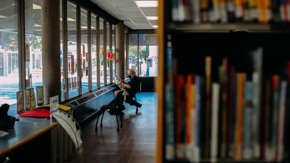 Une personne lit son journal dans une bibliothèque publique.