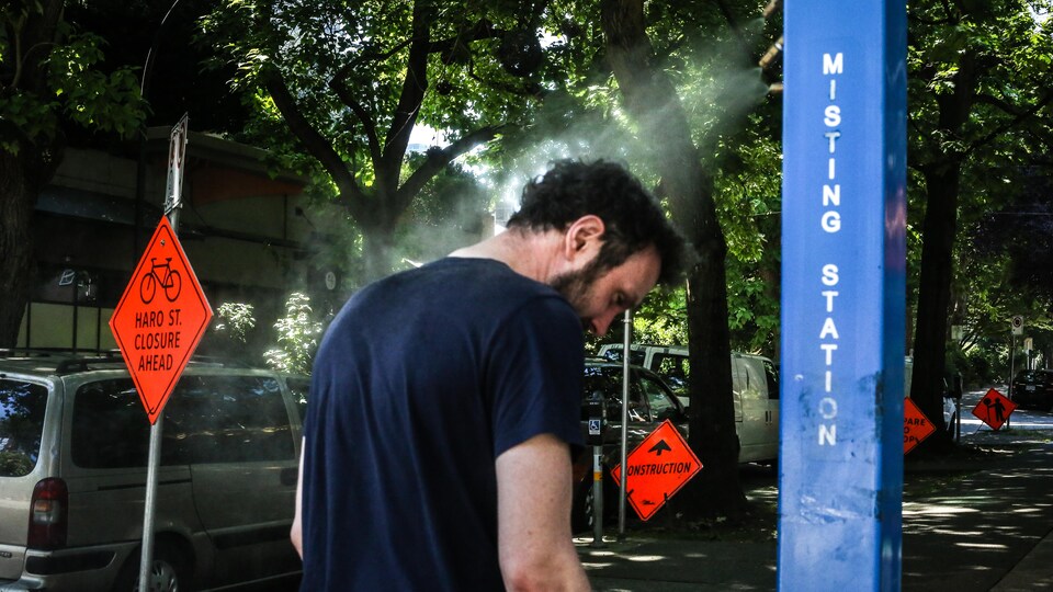 A man uses a fog station to spray his head with water.