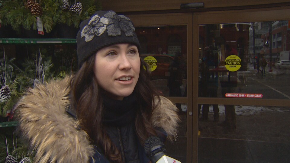 Une femme qui porte une tuque noire, à la porte d'entrée d'un épicerie.