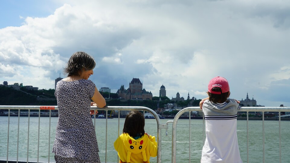 Une mère et ses deux enfants accoudés à une barrière métallique. Ils regardent le fleuve et Québec.