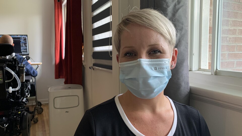 Une femme blonde aux cheveux courts sourit derrière son couvre-visage.