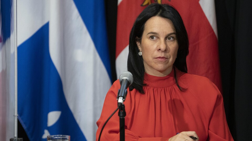 Valérie Plante assise derrière un micro et devant des drapeaux durant une conférence de presse.