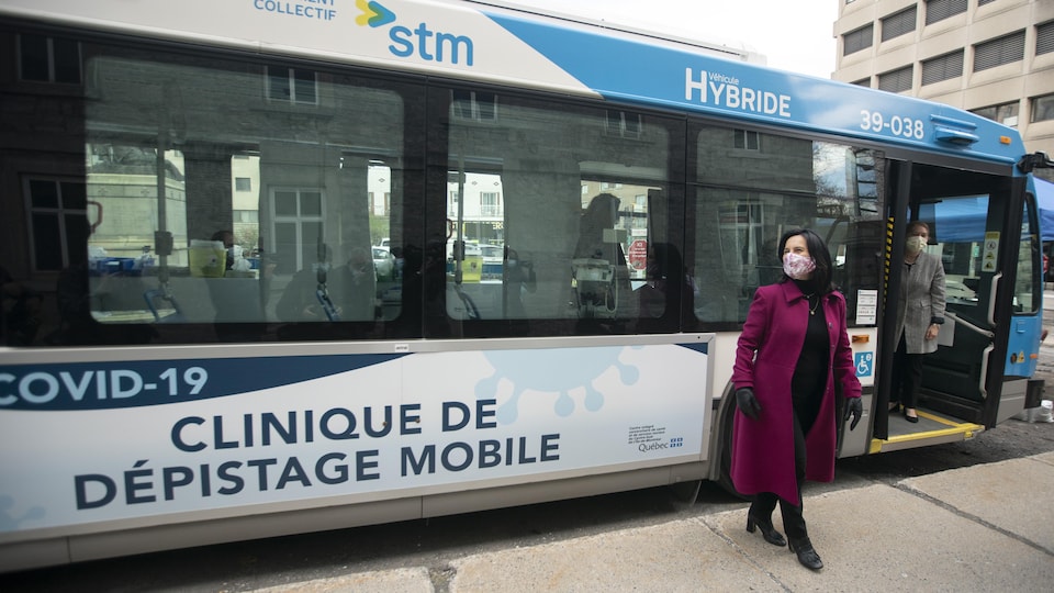Valérie Plante, qui porte un masque, pose devant un autobus de la STM transformé en clinique de dépistage de la COVID-19.