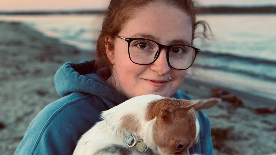 A girl smiles at the camera with a dog in her arms.