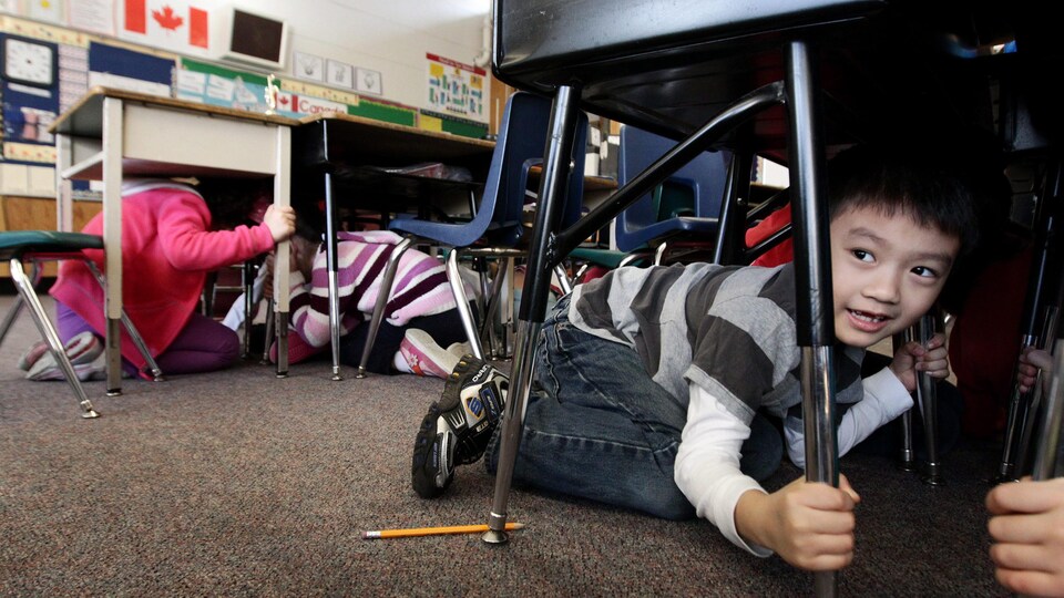 Un élève accroupi sous un pupitre.