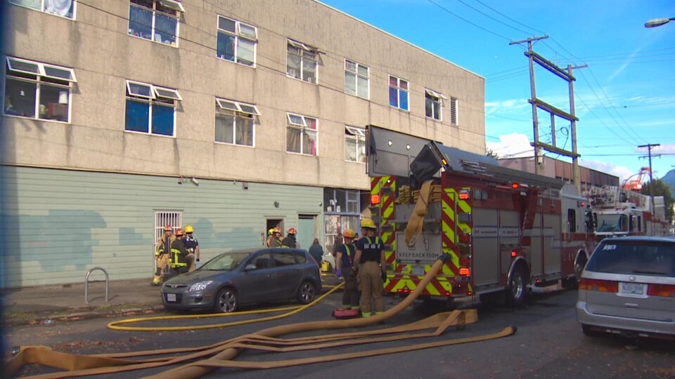 Des lances d'incendie sont déployées depuis un camion de pompiers garé devant un immeuble.