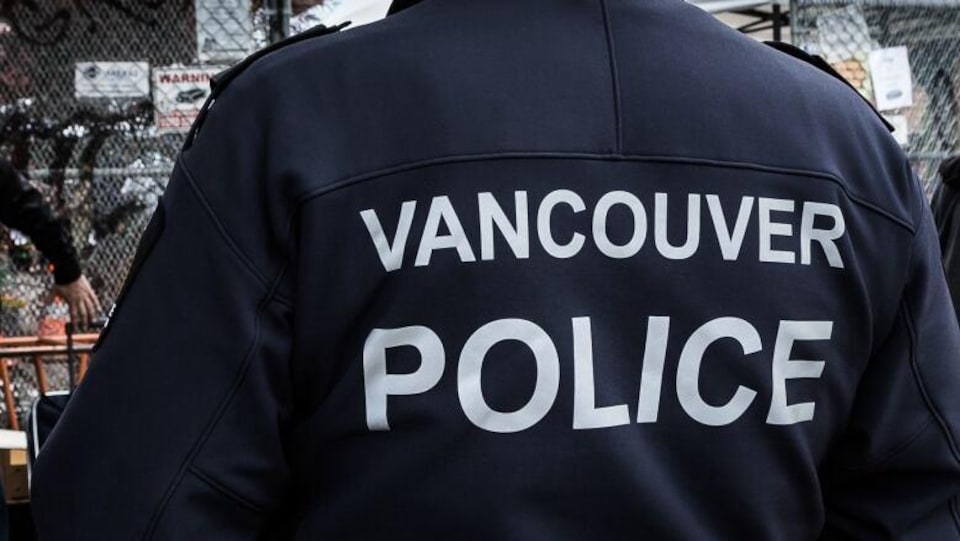Un policier de dos. Il porte un manteau où il est écrit en anglais : police de Vancouver.