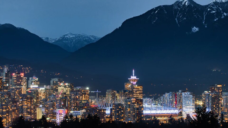 Le centre-ville de Vancouver illuminé à l'approche de la nuit avec d'immenses montagnes au loin.