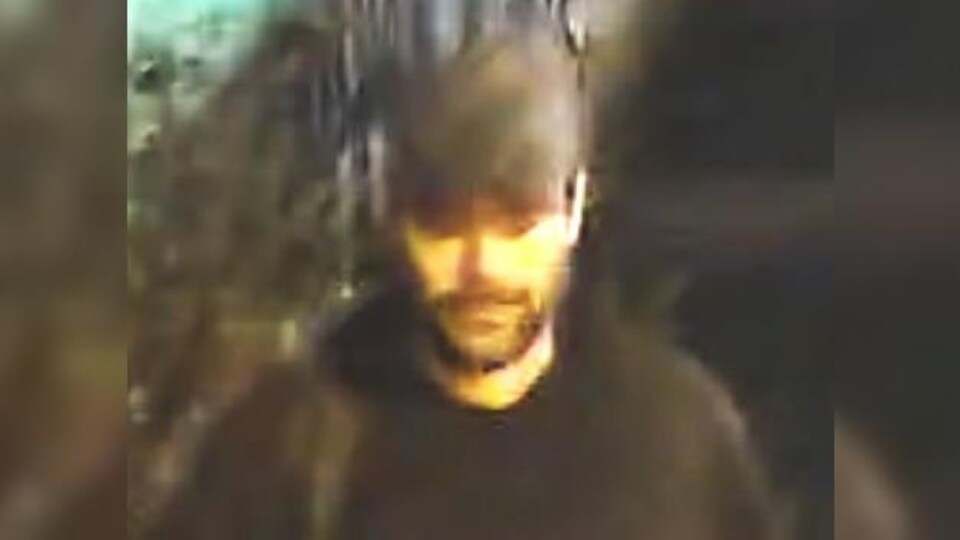 Une capture d'écran de l'homme lors des évènements, il portait une barbe, une casquette, un manteau noir, un pantalon noir, un sac à dos et des bottillons beiges.