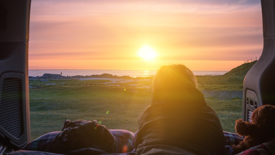Un homme observe le coucher de soleil, allongé à l'intérieur de sa fourgonnette.