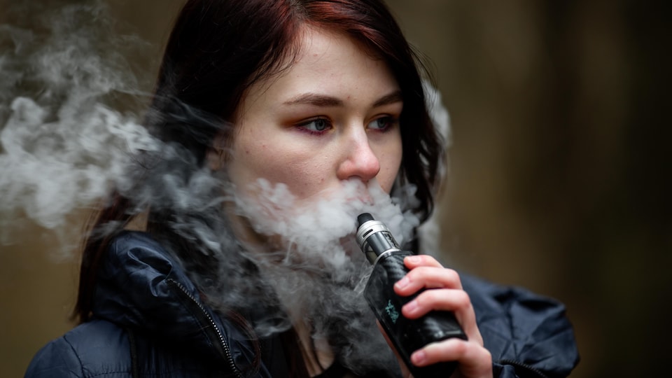 Une jeune femme fume une cigarette électronique.