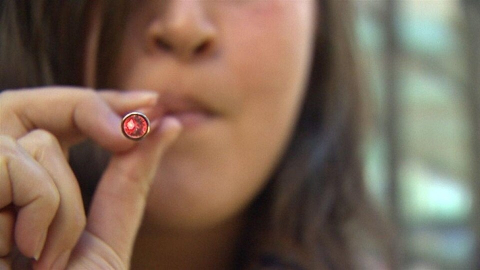 Gros plan sur une cigarette électronique utilisée par une jeune, en flou.