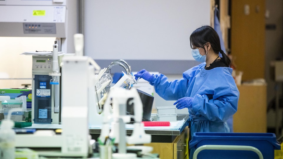 Une technicienne avec un masque devant une machine de séquençage génétique.