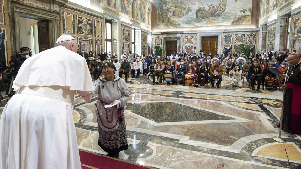 The pope shakes hands with an Inuk woman in front of a full house