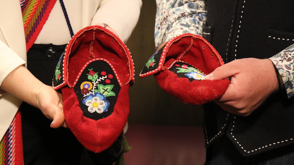 Des mains tiennent deux souliers rouges brodés