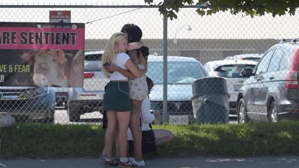 Trois femmes enlacées devant une affiche revendicatrice.