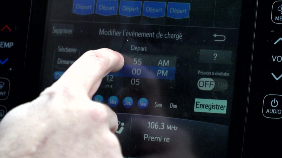 Une main appuie sur l'écran tactile d'un tableau de bord de voiture.