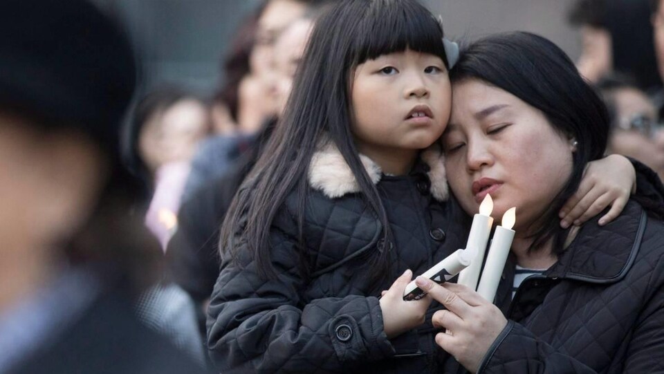 Une femme porte une petite fille et elle tiennent toutes les deux des bougies électriques.