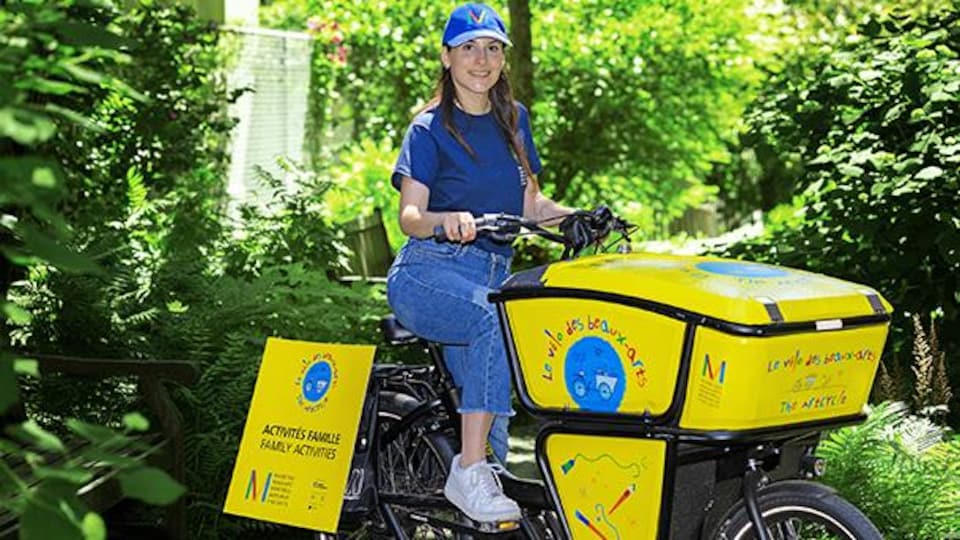 Une femme portant une casquette conduit un vélo-cargo. 
