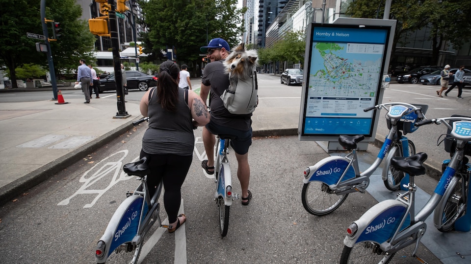 Un homme transporte un chien dans son sac à dos en se déplaçant en vélo sur une piste cyclable du centre-ville de Vancouver.