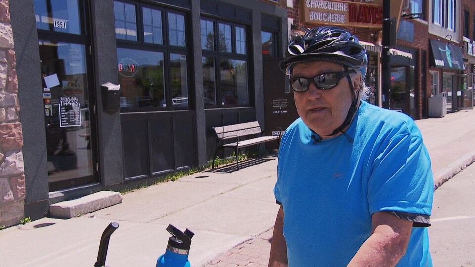 A man on a bicycle wearing a helmet in front of a store.