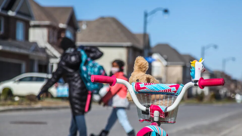 A bicycle parked on a residential street, in the background, two people crossing the street.