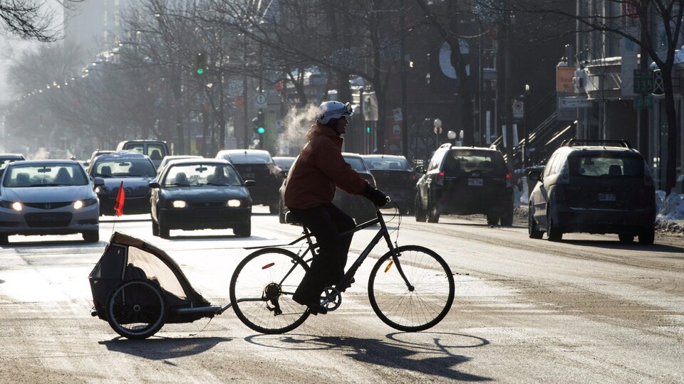 Une cycliste traversant une route occupée avec son bébé à l'arrière du vélo. 