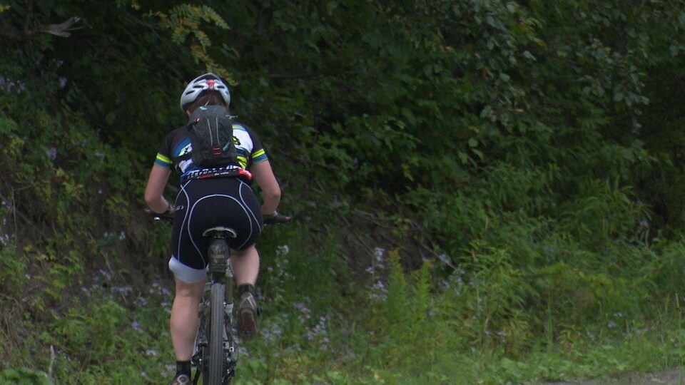 Vue de dos d'un cycliste en vélo de montagne qui s'engage dans un sentier en forêt