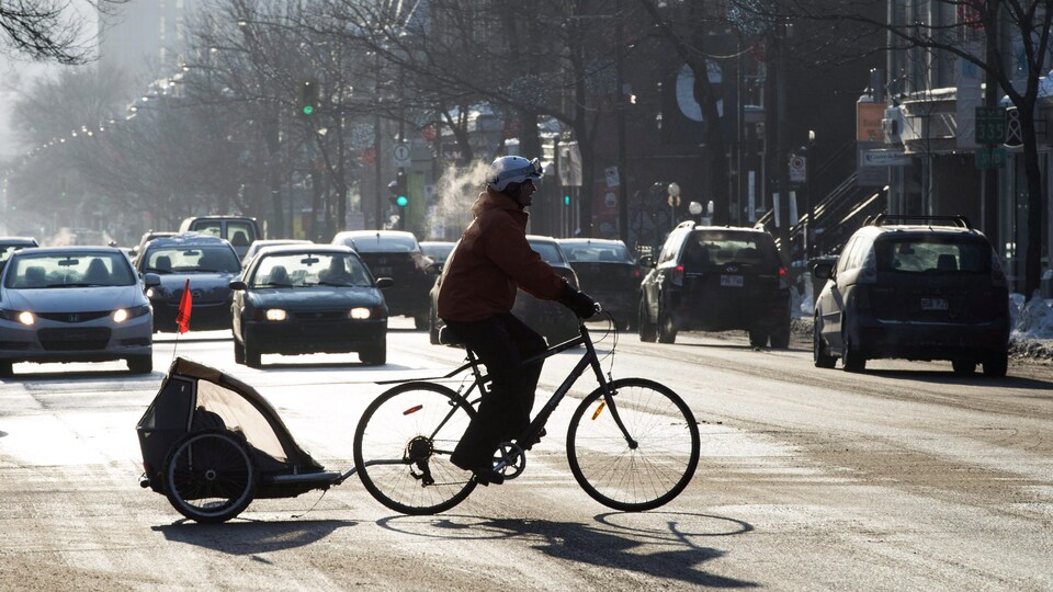 Un cycliste traverse une intersection dans des conditions hivernales, à Montréal.