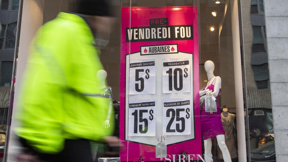 Un passant devant une vitrine de magasin où sont affichées des soldes.