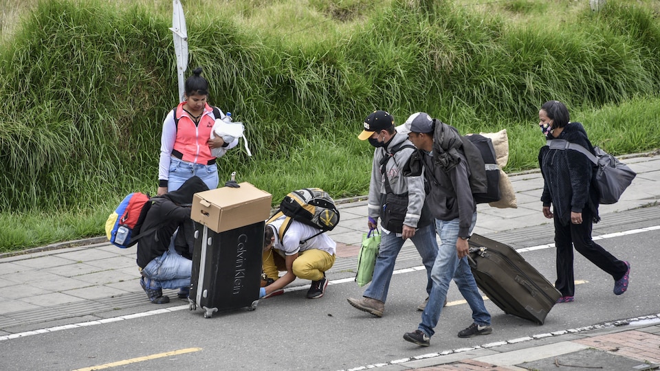 Un groupe d'hommes et de femmes au milieu d'une route portant des bagages.