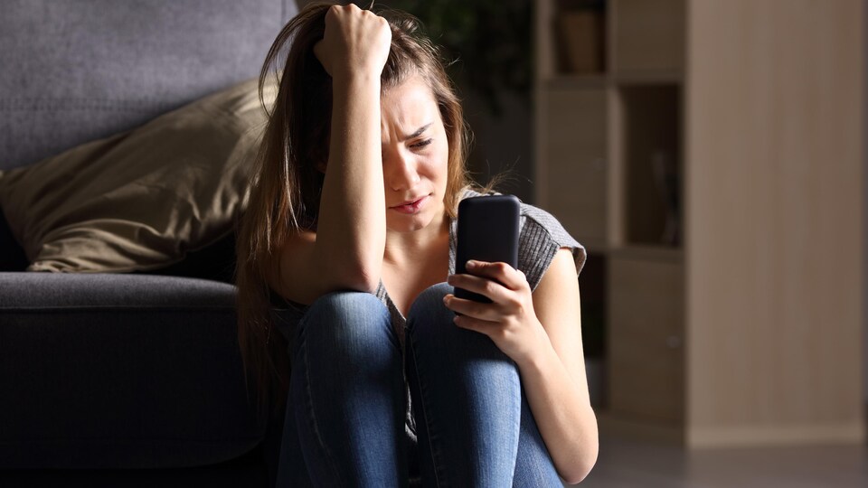 Une jeune femme préoccupée fixe son téléphone cellulaire.