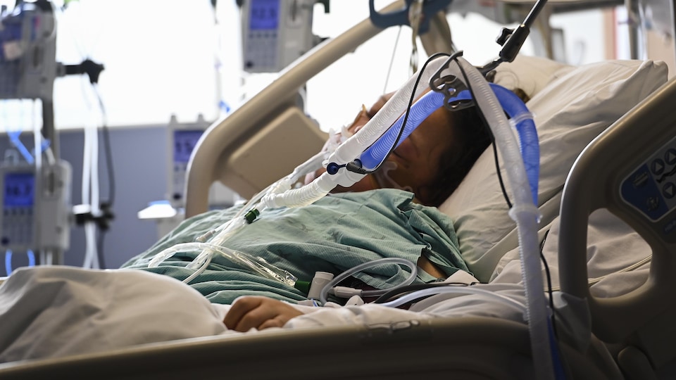 Une femme sous respirateur, couchée dans un lit d'hôpital.