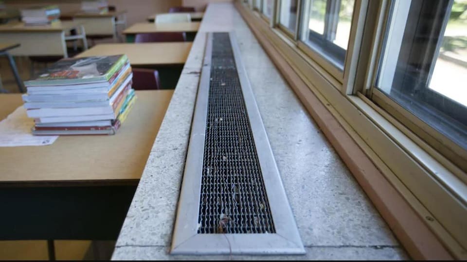 Une pile de livres sur un pupitre près de fenêtres dans une classe.