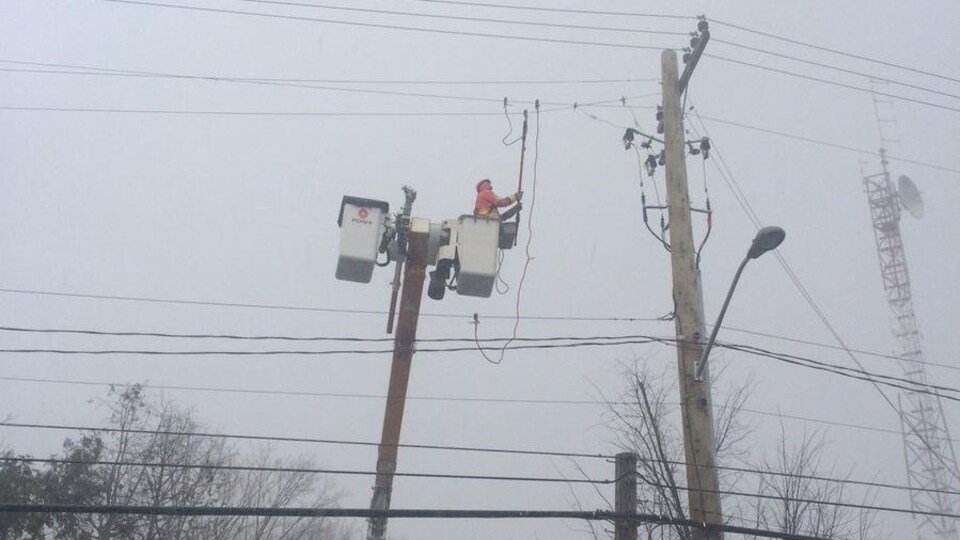 Une personne travaille dans une nacelle près d'un poteau électrique.