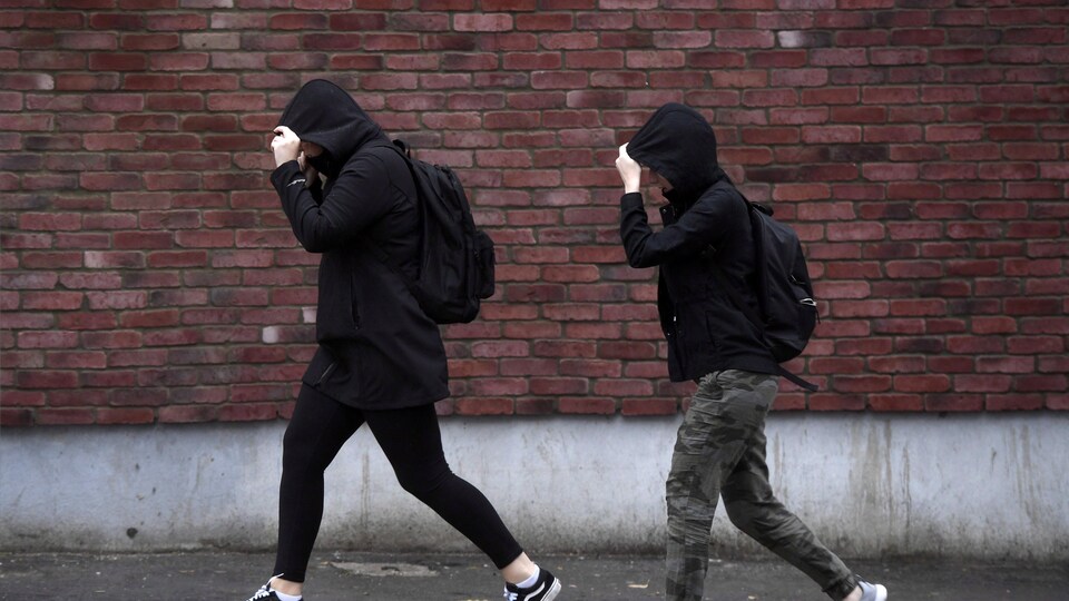 Des piétons se couvrent le visage en marchant sous la pluie à Ottawa.