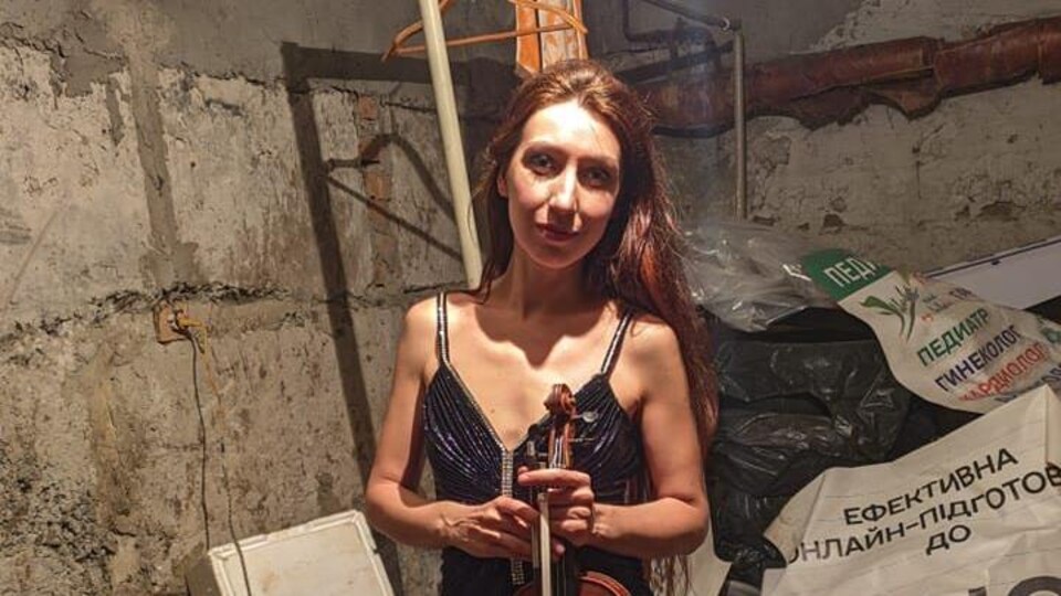 Une femme dans un sous-sol non fini tient son violon.