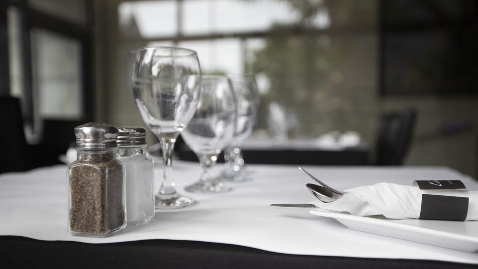 Des verres, une salière, une poivrière et des ustensiles sont disposés sur une table.