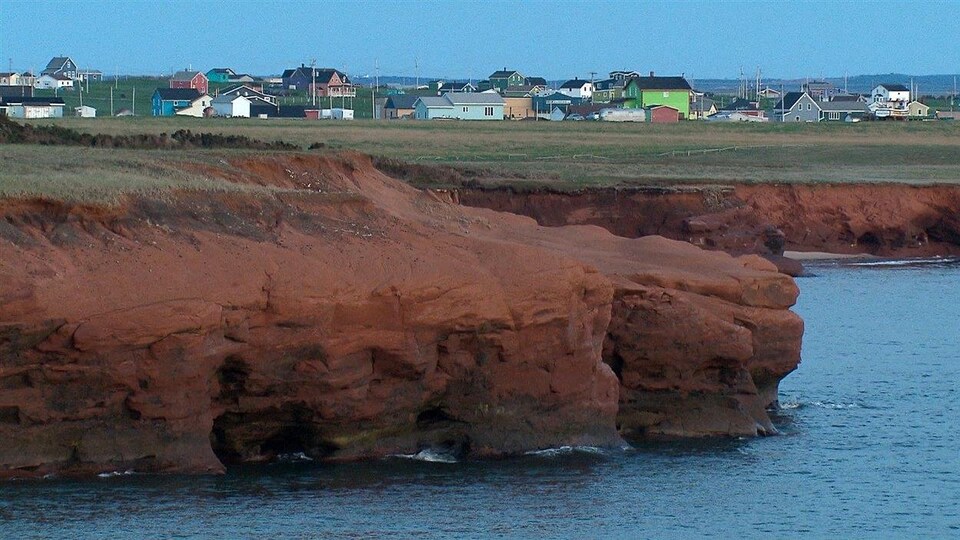 Une berge sablonneuse des Îles-de-la-Madeleine avec des maisons colorées en arrière-plan.