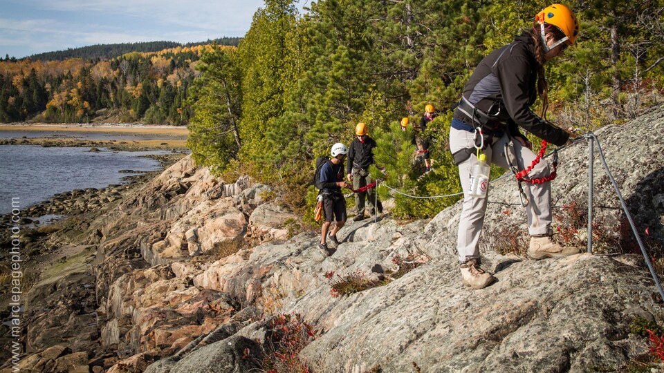 Des escaladeurs sur une paroi rocheuse, un lac et la forêt en arrière-plan.