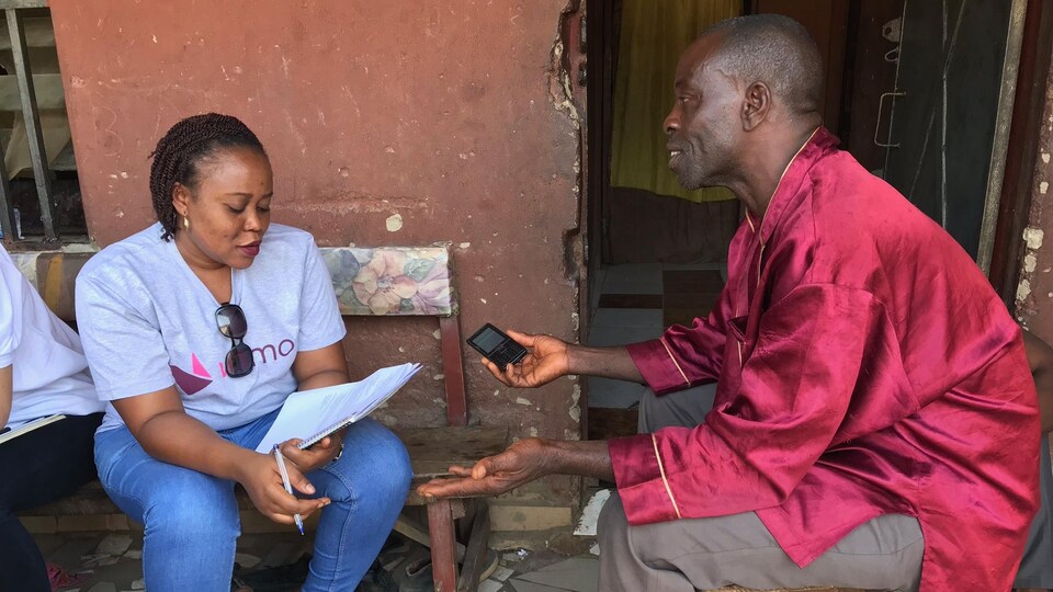 Une dame tenant un calepin de notes conseille un homme vêtu de rouge avec un téléphone cellulaire à la main.