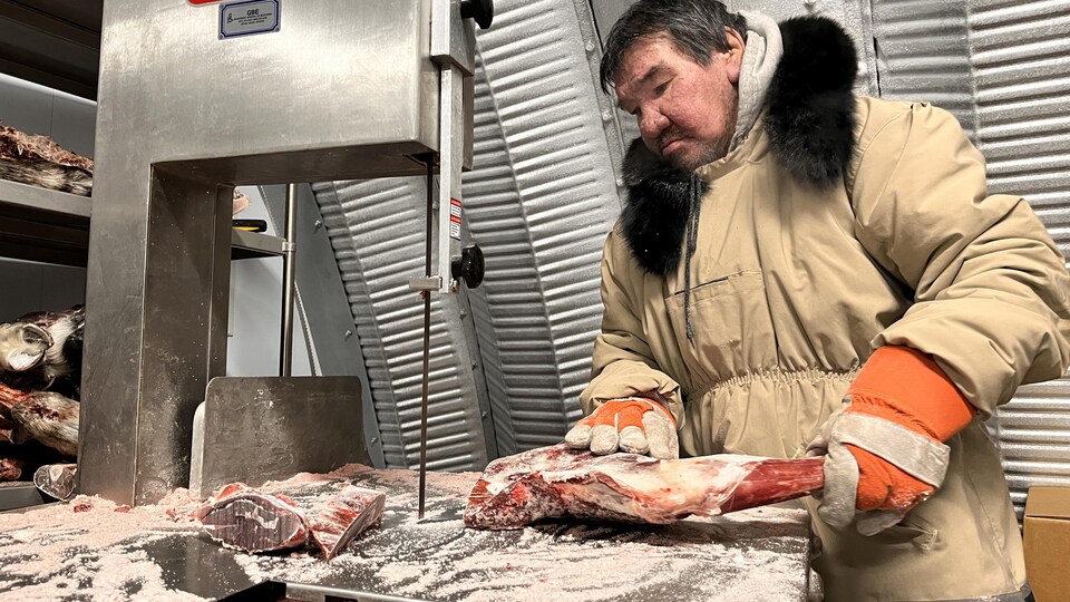 Un homme manipule une pièce de viande avec une scie à ruban. 