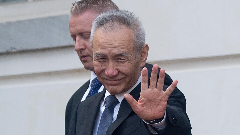 Le vice premier ministre chinois Liu He saluant la caméra, alors qu'il est accompagné d'un autre homme, les deux portant un veston-cravate.