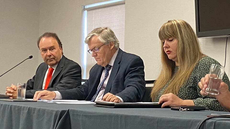 Me Marc Bellemare, Me Alain Arsenault et Shirley Christensen assis derrière une table lors d'une conférence de presse.