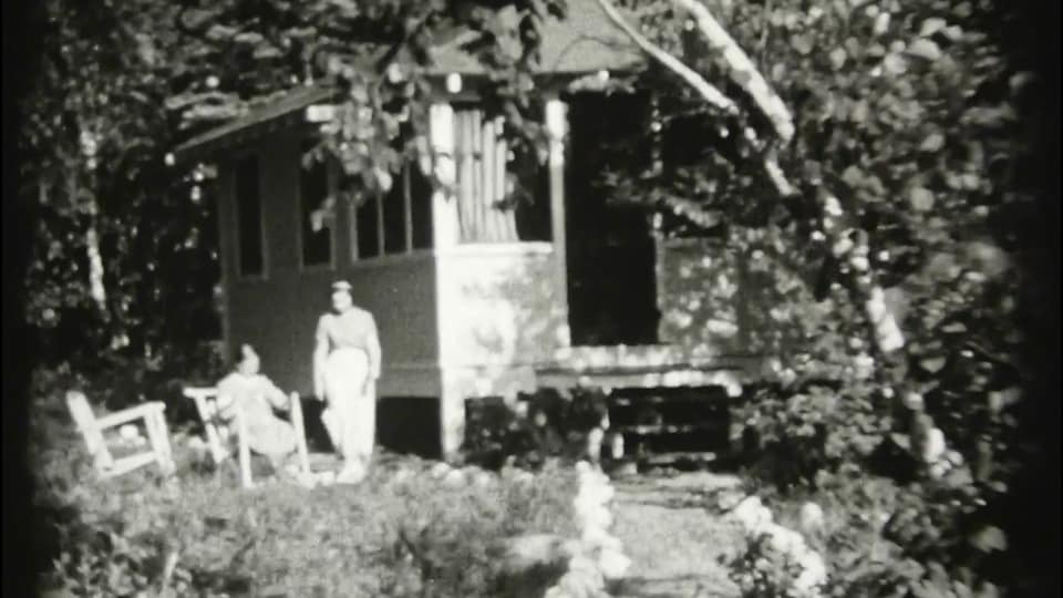 Image d'archive d'un chalet à côté duquel deux personnes se trouvent.