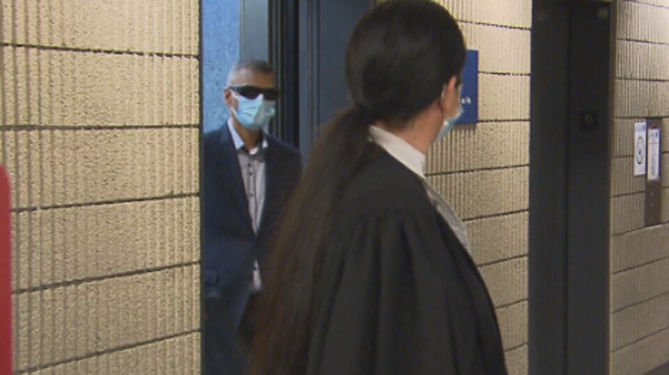 Victorio Reno Pereira, portant un masque et des lunettes de soleil, sort d'une salle au palais de justice, tandis qu'on voit son avocate dans le corridor.