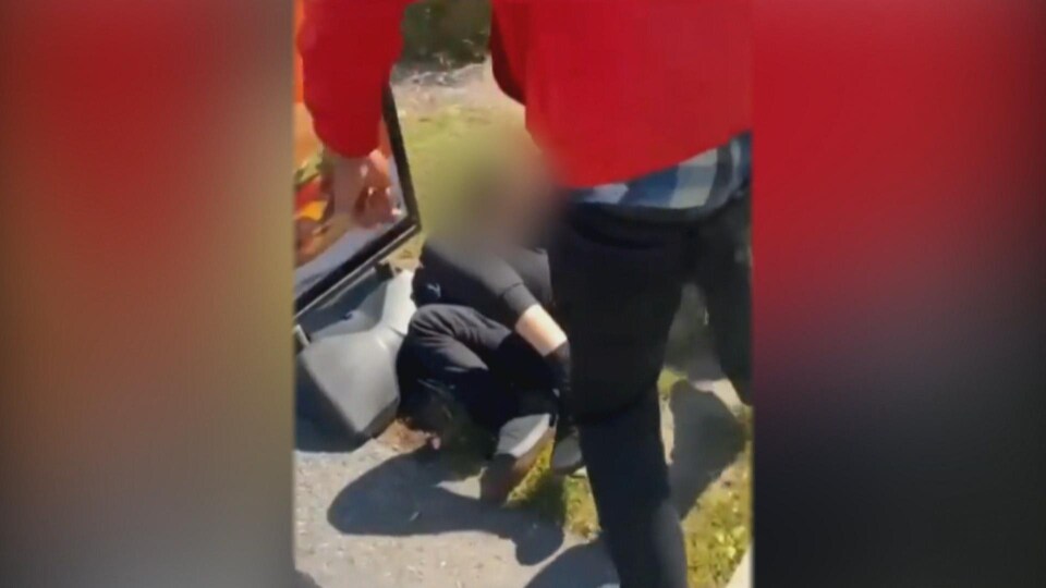 Une capture d'écran de la vidéo qui montre un adolescent se faire tabasser. Celui-ci est au sol. Un jeune portant un chandail rouge, poing demi-serré, se tient debout devant lui.