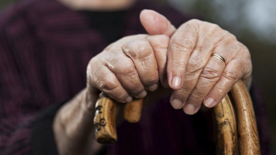 Les mains d'une personne âgée tiennent une canne. 