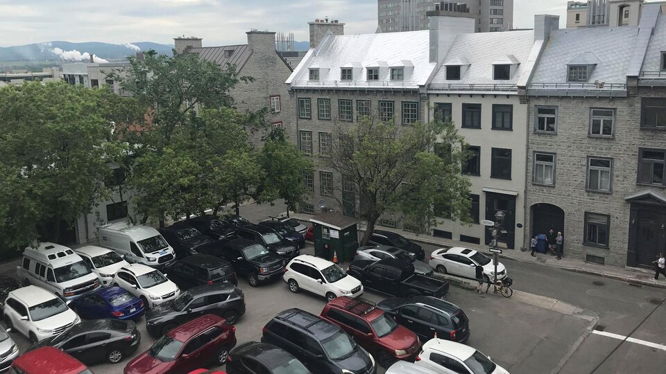 Au premier plan, on peut voir des dizaines de voitures stationnées. Ensuite, on peut voir des édifices de trois étages et des lucarnes.